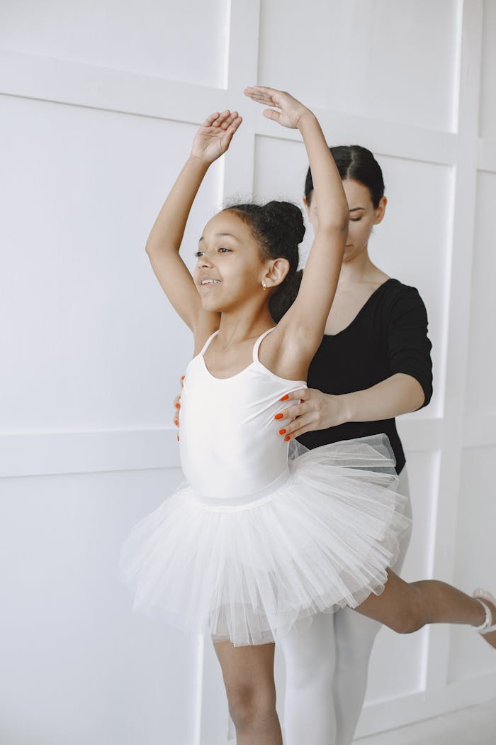 A young girl in a tutu being guided by an instructor in an elegant dance pose.