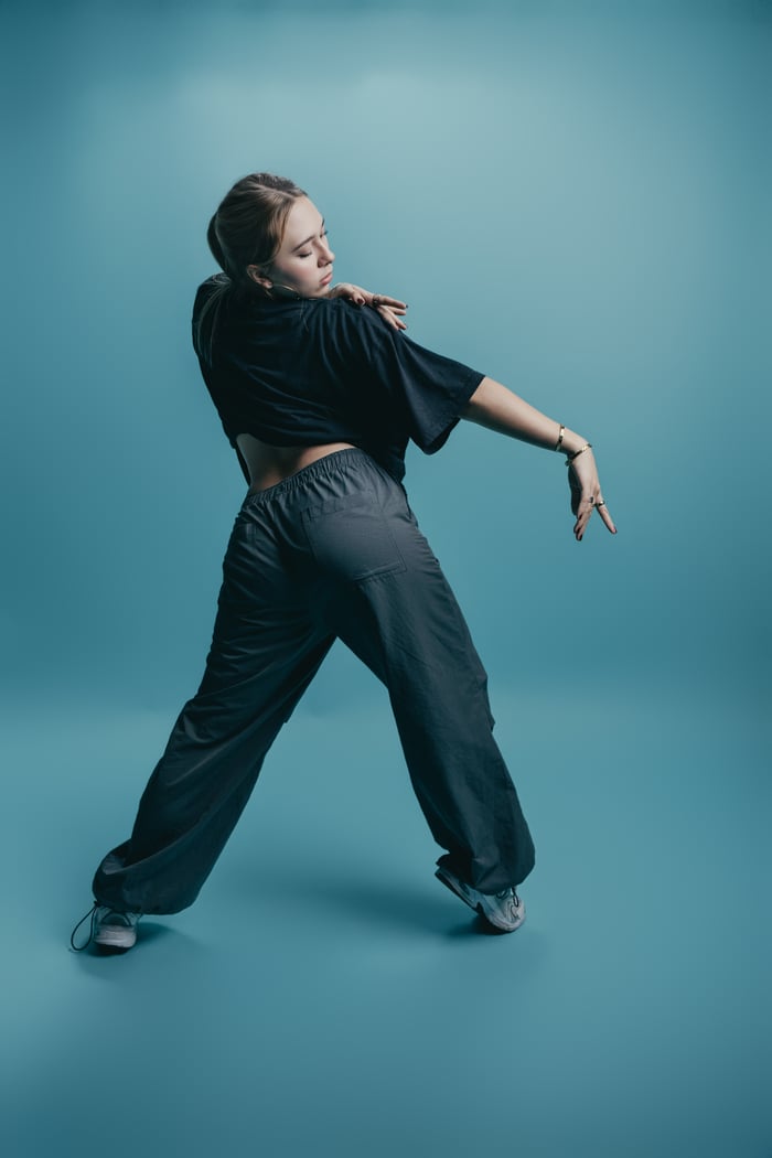 A dancer striking a dynamic pose in a studio with a blue background, showcasing modern dance movements.