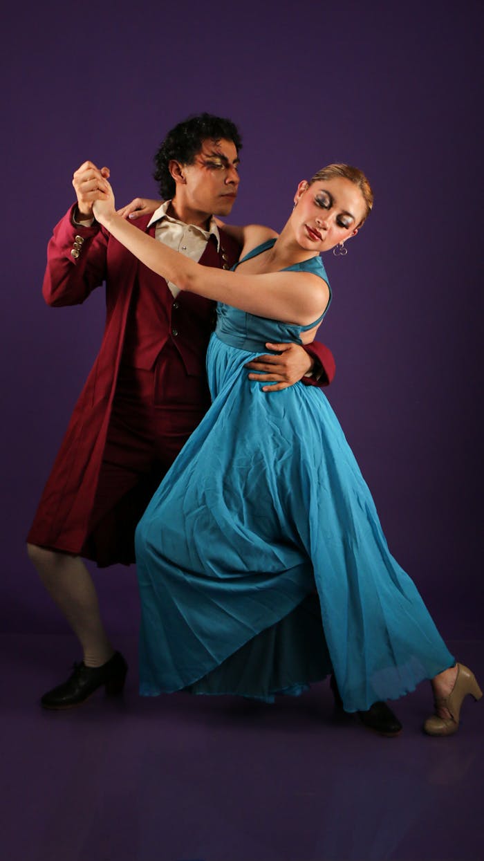 A couple in elegant attire performs a passionate dance against a purple background.